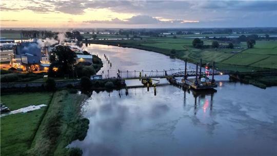Die Eisenbahnbrücke am Abend nach dem Unfall: Züge fahren nicht mehr, ein Teil des Brückenüberbaus hängt fast im Wasser, die Oberleitungsmasten sind verbogen. Foto: Lars Penning