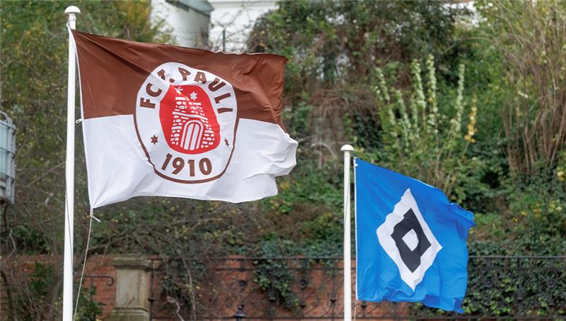Termin für Stadtderby zwischen HSV und St. Pauli steht fest Die Fahnen der beiden Hamburger Bundesliga Profi-Fussballclubs wehen nebeneinander an zwei Masten. Foto: Markus Scholz/dpa