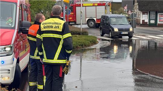 Einsatzkräfte der Feuerwehr stehen vor dem überfluteten Kreisel in Jork.