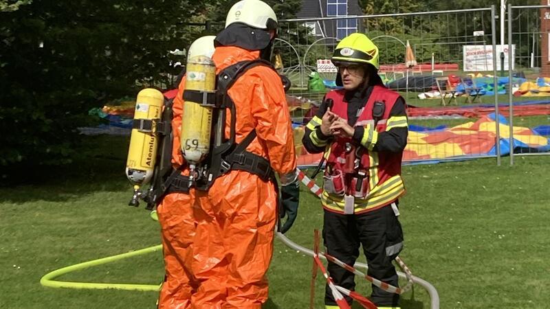 Zwei Feuerwehrleute in Chemikalien-Schutzanzügen stehen auf einer Wiese.