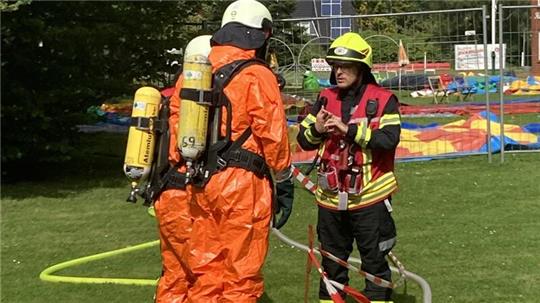 Zwei Feuerwehrleute in Chemikalien-Schutzanzügen stehen auf einer Wiese.