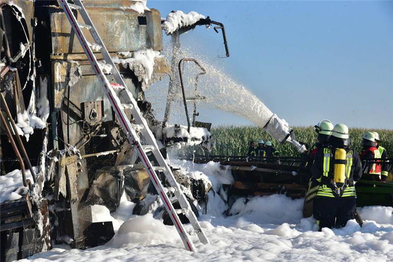 Die Feuerwehrleute legen einen Schaumteppich über den brennenden Mähdrescher. Foto: Beneke