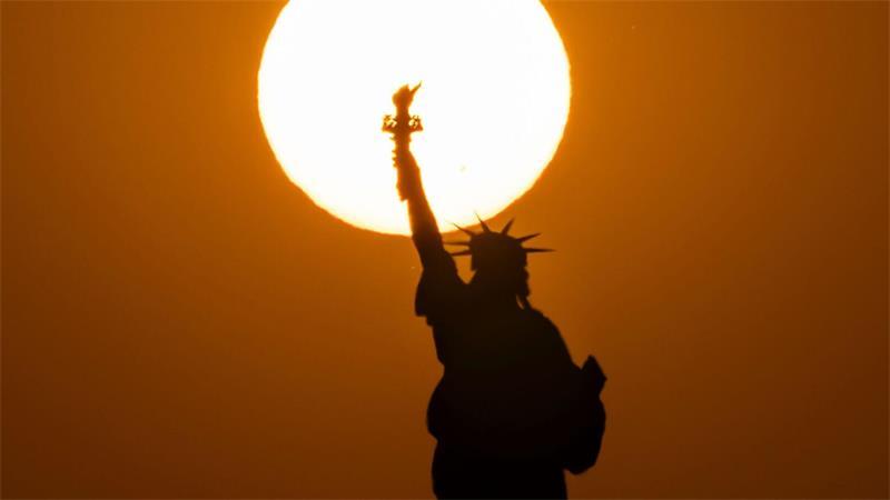 Die Freiheitsstatue in New York zeichnet sich vor der untergehenden Sonne ab.