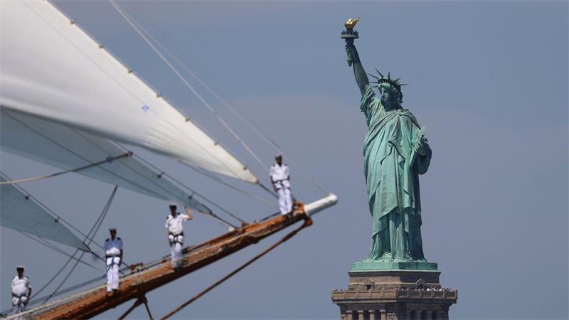 Die Freiheitsstatue ist zu sehen, während Seeleute eines Großseglers vorbeisegeln.