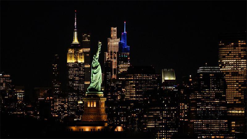 Die Freiheitsstatue steht bei Nacht vor der Skyline von Manhatten.