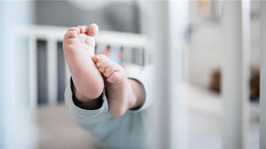 Die Füße eines Babys sind in einem Kinderbett zu sehen.