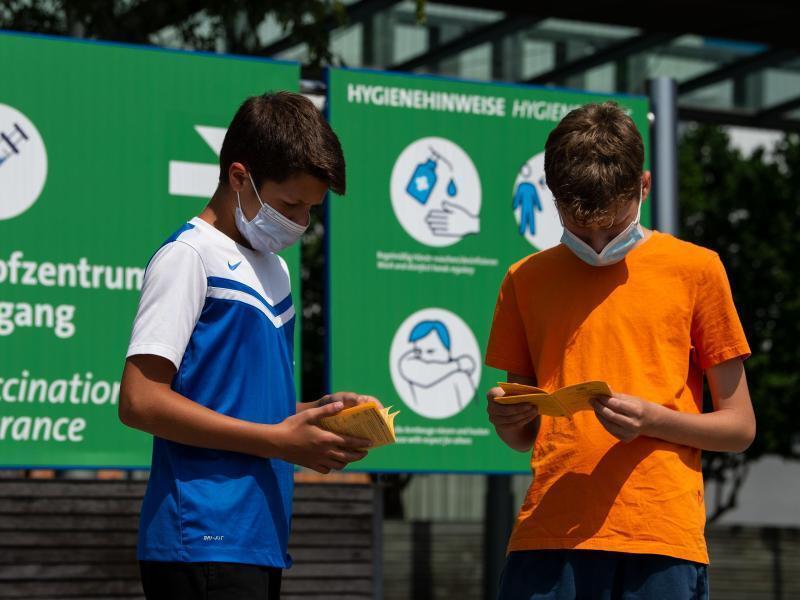 Die Geschwister-Impflinge Hugo (12 Jahre) und Urs (13 Jahre) blättern vor ihrer Impfung am Impfzentrum auf dem Messegelände in ihren Impfbüchern. Foto: Swen Pförtner/dpa