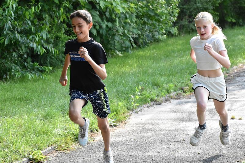 Ein Schüler und eine Schülerin laufen auf einer Laufbahn und haben Spaß dabei.