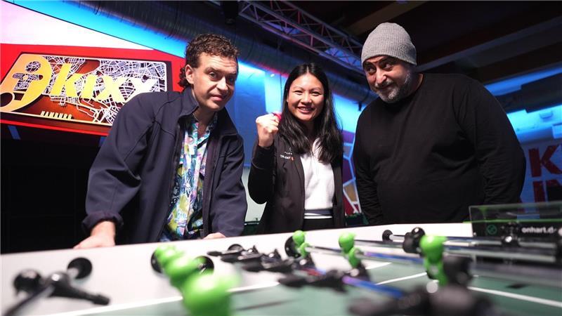 Die Großstadtrevier-Schauspieler Özgür Karadeniz und Enrique Fiß stehen neben Linh Tran, Weltmeisterin im Tischkicker.