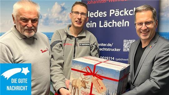 Die Johanniter-Einsatzkräfte Hansi Eggert und Kevin Heckmann nehmen von Landrat Kai Seefried ein Paket für die Weihnachtstrucker-Aktion entgegen.