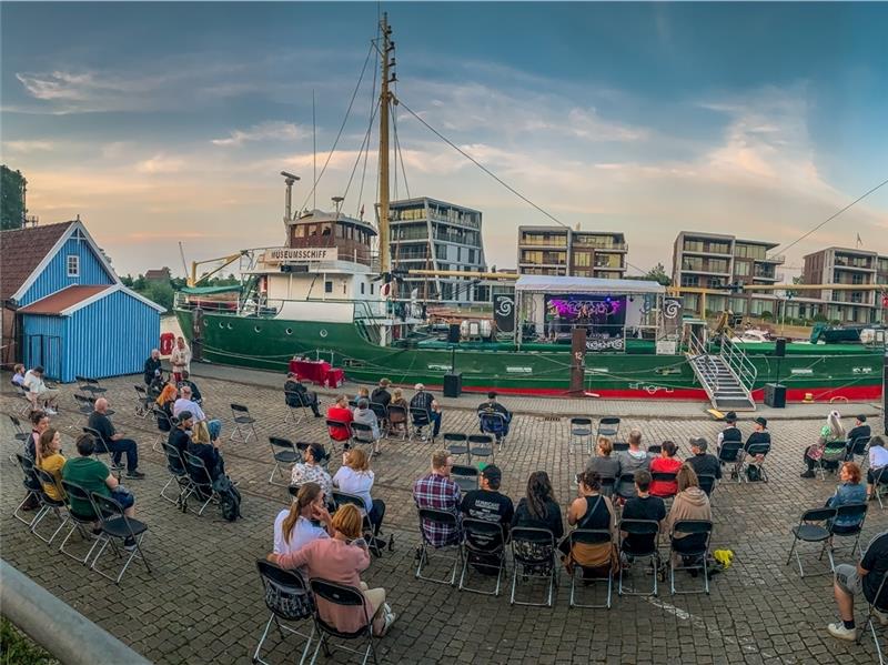 Die Live-Musik kommt von Bord der „Greundiek,“ auf dem Stadthafen- Parkplatz sitzen die Zuhörer. Foto: Stade Marketing