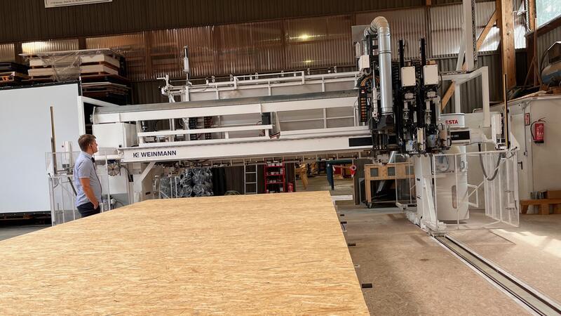 Handwerk mit Wow-Effekt: Bei Hölting baut Maschine ganze Hauswände Die Multifunktionsbrücke fährt über das Material auf dem Fertigungstisch, nagelt die Platten auf die Balken darunter, sägt Fensteröffnungen aus und glättet Konturen.