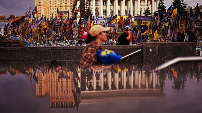 Die Nationale Musikakademie (r) spiegelt sich in einem U-Bahn-Eingang am Unabhängigkeitsplatz in Kiew wider, wo ukrainische Flaggen und Fotos zum Gedenken an die im Krieg mit Russland getöteten Zivilisten und Soldaten aufgestellt sind.