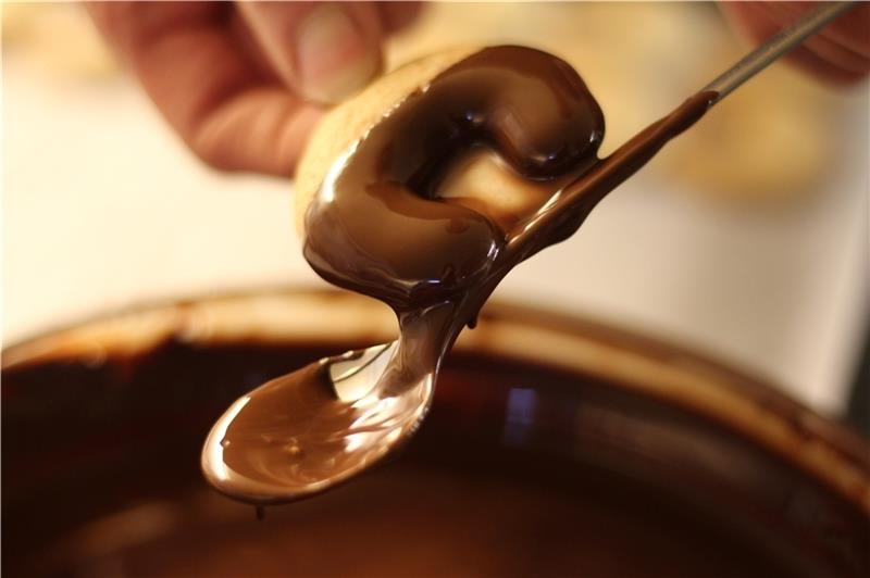 Die Nusskipferln werden zum Abschluss in Schokolade getaucht. Mit dem Stiel eines langen Löffels wird die überschüssige Schokolade abgezogen. Fotos: Frank