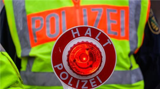 Ein Polizist hält während einer Verkehrskontrolle eine Polizeikelle in der Hand.