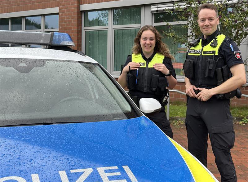 Die Polizeikommissare Schulze (links) und Schunk erzählen an ihrem Stand über Arbeitsalltag, Studium und Voraussetzungen. Vor der Halle parkt ein Streifenwagen.