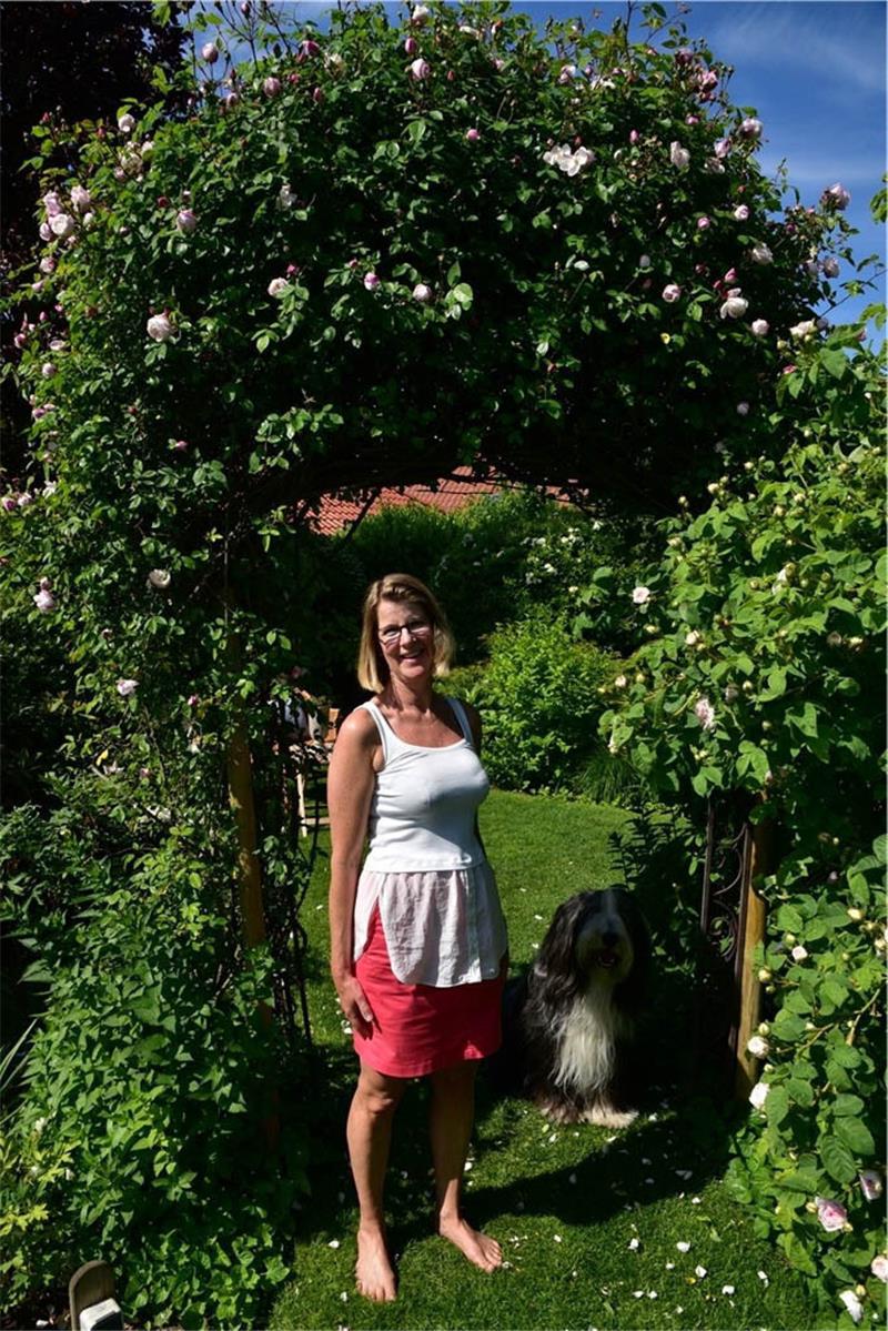 Die Rosen am Bogen, unter dem Anja Preuß mit Hund Vincent steht, sind so kräftig, dass die Konstruktion abgestützt werden muss. Fotos: Beneke