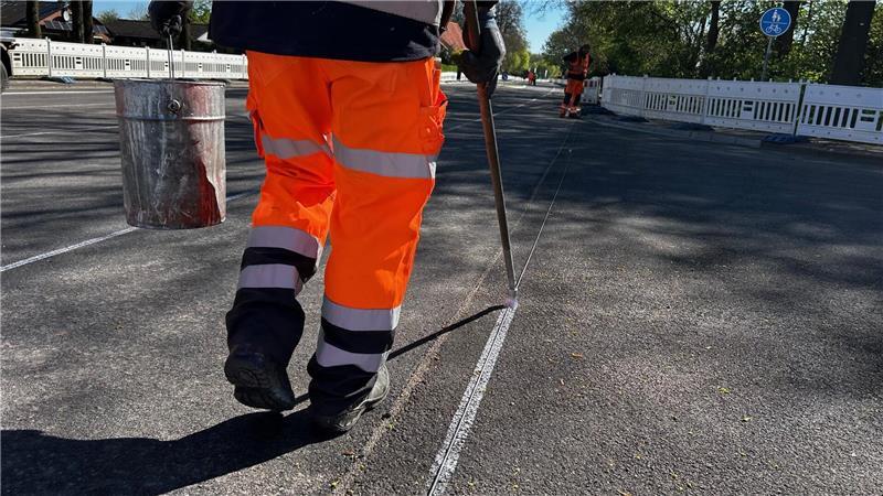 Die Schnur gibt die Linie vor, der Pinsel hält sie fest. Die silber glänzende Farbe funktioniert als Vorzeichnung für die eigentliche Fahrbahnmarkierung.