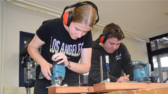 Die Schülerfirma stellt eine Sitzbank her. Hier sägt Romy (15). Lukas (15) zeichnet die nächsten Schnitte an.