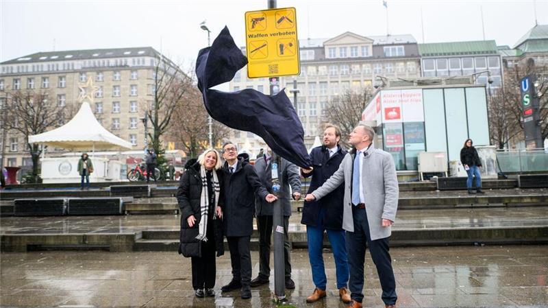 Waffenverbot in Hamburg bleibt dauerhaft – Ausnahmen und Strafen Die Senatoren Anjes Tjarks (2.v.r.; Grüne) und Andy Grote (rechts; SPD) enthüllen am Jungferstieg ein Schild, welches auf das Waffenverbot hinweist.