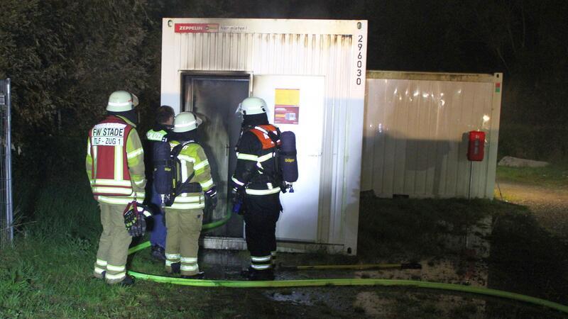 Feuer in Stader Flüchtlingsunterkunft - 30.000 Euro Schaden Drei Feuerwehrleute und ein Polizist stehen vor dem ausgebrannten Container.
