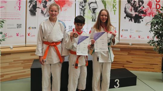Schamschad Hahn und Emilia Guse in weißem Judoka-Mantel präsentieren ihre Medaille und eine Urkunde.