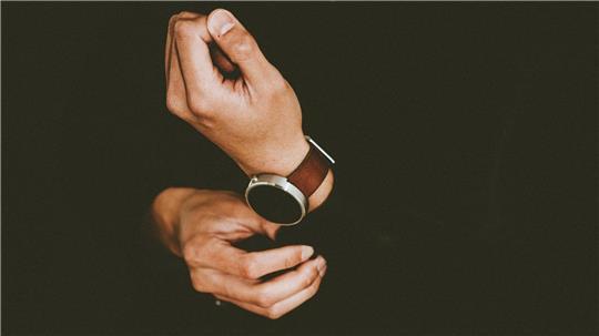 Eine Hand greift nach einer Armbanduhr.