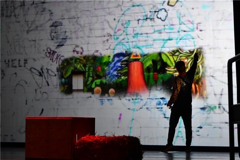 Stadeum-Publikum feiert rappenden Papageno Die Szenerie wird einfach über eine riesige Leinwand projiziert, die von der Graffitiwand zur Dschungellandschaft oder Feuersbrunst wird.