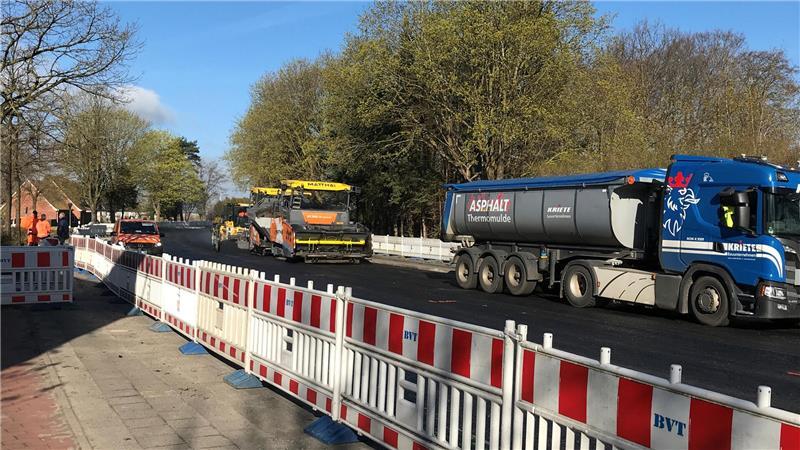 Die Thermomulche fährt vorweg und lässt das Asphaltgemisch auf die Tragschicht fließen. Der Asphaltfertiger dahinter verteilt mit Förderschnecken das160 Grad heiße Gemisch. Dahinter fährt eine Walze und verdichtet das Gemisch.