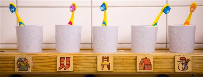 Die Zahnbürsten der Kinder einer Kita stehen in Zahnputzbechern auf einem Regal im Badezimmer. In Hamburgs Kitas wird sich mehr Personal um die Kinder kümmern. Foto Charisius/dpa