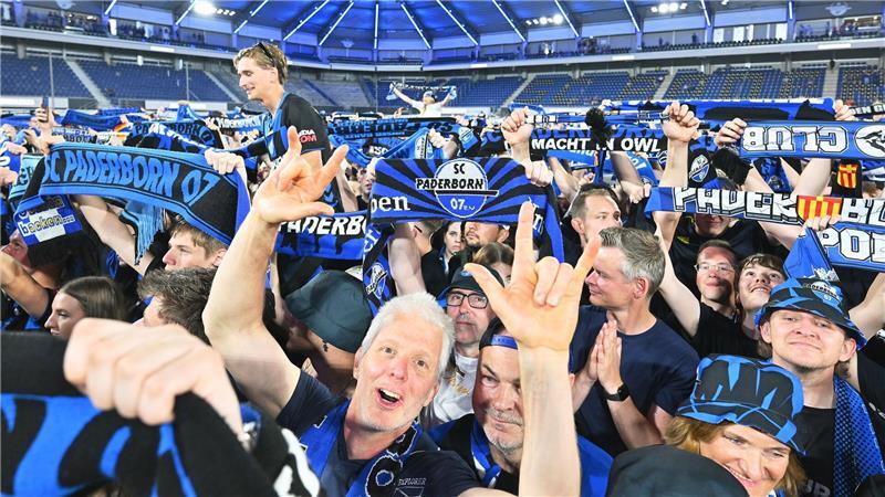 Die Zuschauer im Stadion feiern und halten Schals in die Höhe.