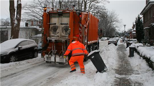 Ein Müllwerker zieht im Schnee eine Tonne zum Müllfahrzeug.