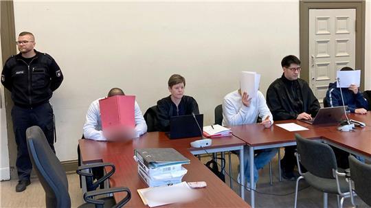 Die drei wegen versuchten Mordes angeklagten Männer verbergen ihre Gesichter vor den Kameras der Pressevertreter.