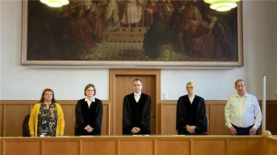 Die ehrenamtlichen und Berufsrichter der I. Großen Strafkammer Flensburg stehen vor der Urteilsverkündung in einem Saal des Landgerichts.