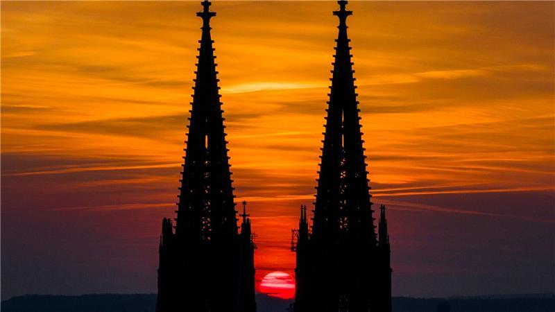 Die untergehende Sonne lässt den Himmel hinter dem Kölner Dom in orange-rot leuchten.