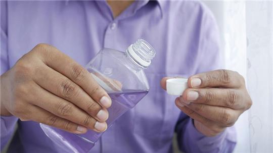 Ein Mann hält eine Flasche Mundspüllösung in der Hand.