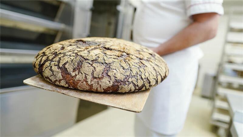 Ein Bäckermeister nimmt in einer Backstube der Akademie Deutsches Bäckerhandwerk ein Roggenbrot aus einem Ofen. 