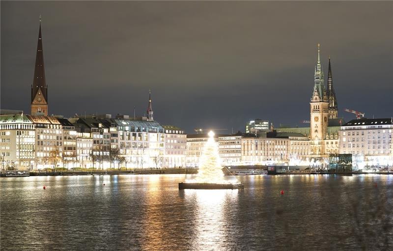 Die Alstertanne leuchtet auf der Binnenalster. Im Hintergrund sind das Rathaus (rechts) und der Michel zu sehen. Foto: Marcus Brandt/dpa