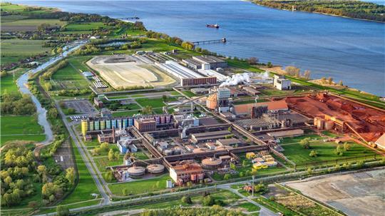 Direkt an der Elbe liegt das AOS-Werk; rechts das rote Bauxit, das zu Aluminiumoxid verarbeitet wird. Auf der sandigen Fläche könnte das Holzkraftwerk entstehen.