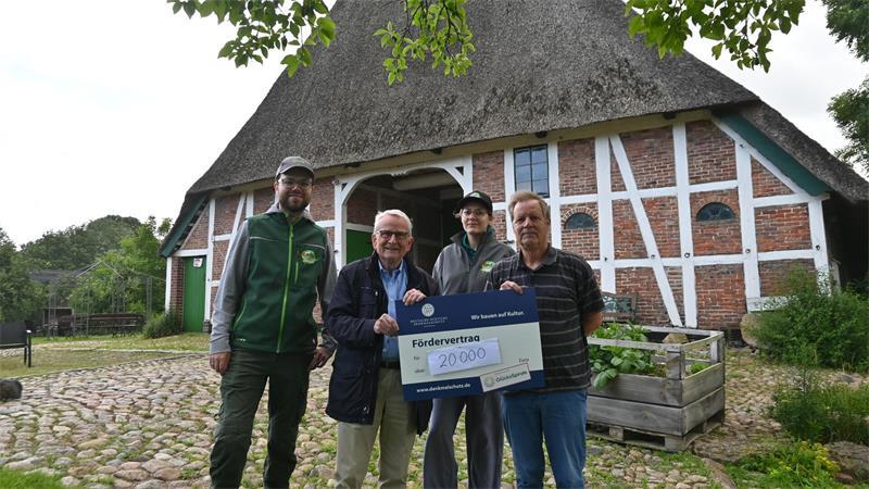 Dr. Reinhold Kolck, Ortskurator Stade der Deutschen Stiftung Denkmalschutz überreicht Henrik und Frauke Köpke und Heinrich Stölken symbolisch den Förderbetrag vor dem Harmshof in Königreich.