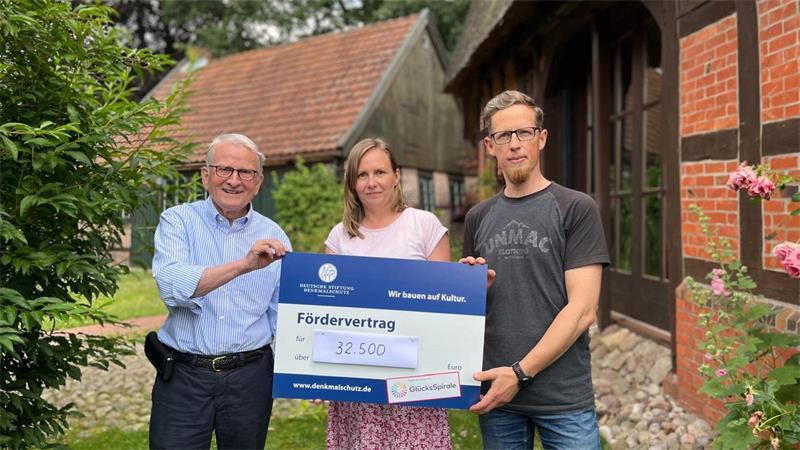 „Jeder Balken hat Geschichte“: Issendorfer Paar belebt alte Schmiede neu Dr. Reinhold Kolck von der Deutschen Stiftung Denkmalschutz (links) übergibt die Fördersumme von 32.500 Euro symbolisch an Maria und Christopher Hubbe.