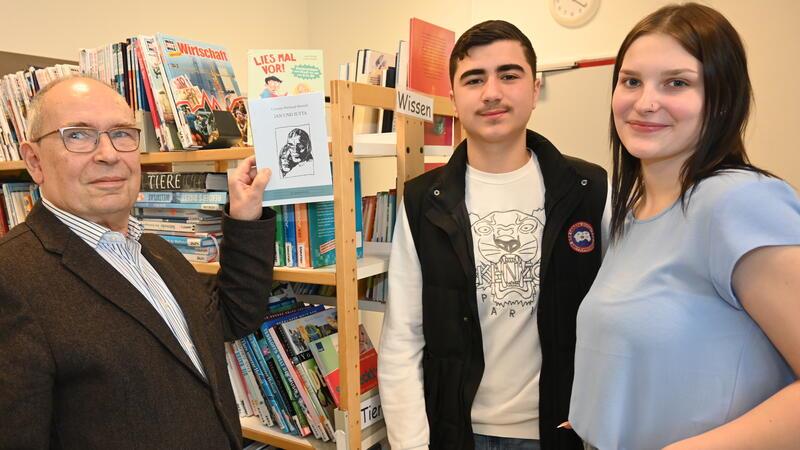 Dr. Rudolf Welskopf schenkt der Schulbücherei ein Exemplar von „Jan und Jutta“, Abdullah Saracan und Anastacia Knop nehmen es stellvertretend in Empfang.