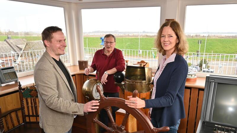 Dr. Sebastian Ipach von der Maritimen Landschaft Unterelbe und Ines Utecht vom Tourismusverband haben das Ruder in der früheren Seefahrtschule fest in der Hand; Kapitän Joachim Brill (Mitte) zeigt Gästen die Brücke.