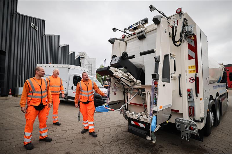 Drei Mitarbeiter der Stadtreinigung Hamburg (SRH) stehen an einem neuen Müllfahrzeug bei einem Pressetermin auf dem Betriebshof. Foto: Christian Charisius/dpa