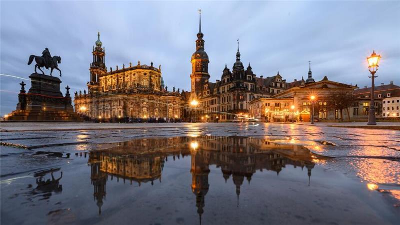Dresden am Abend - Das Reiterstandbild König Johann (l-r), die Hofkirche, der Hausmannsturm, das Residenzschloss und die Schinkelwache spiegeln sich am Abend in einer Pfütze auf dem Theaterplatz.