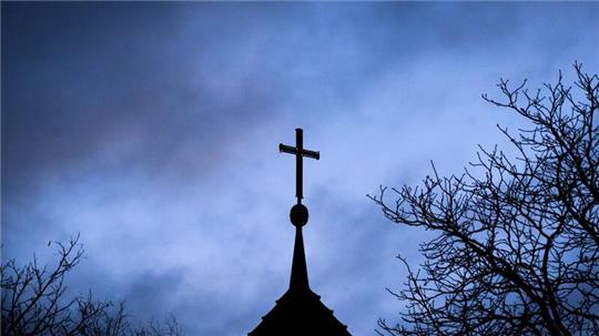 Dunkle Wolken über einem Kreuz einer Kirche: Einem der Opfer muss dSchadenersatz gezahlt werden (Symbolbild).