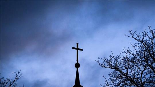 Dunkle Wolken ziehen über das Kreuz auf einer evangelischen Kirche in der Region Hannover.