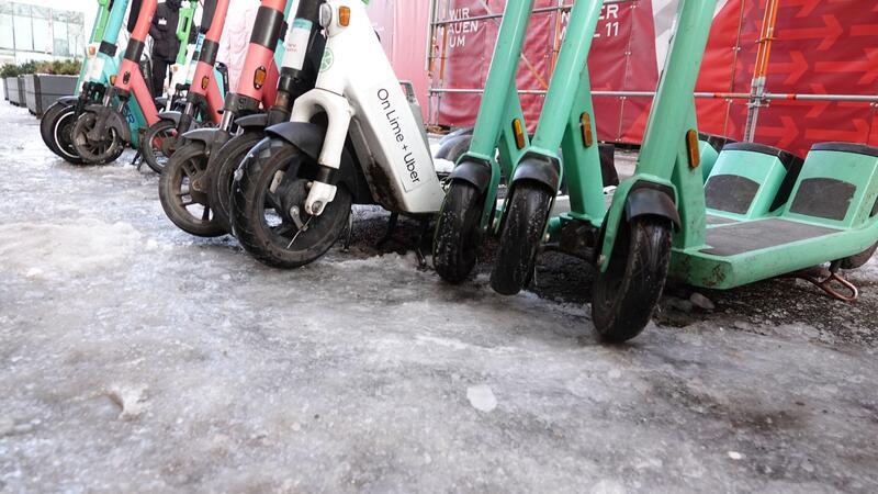 E-Scooter stehen an einem vereisten Gehweg in der Innenstadt.
