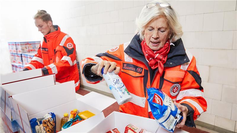 Ehrenamtliche Helfer der Johanniter befüllen Weihnachtstrucker-Pakete mit Lebensmitteln und Hygieneartikeln.
