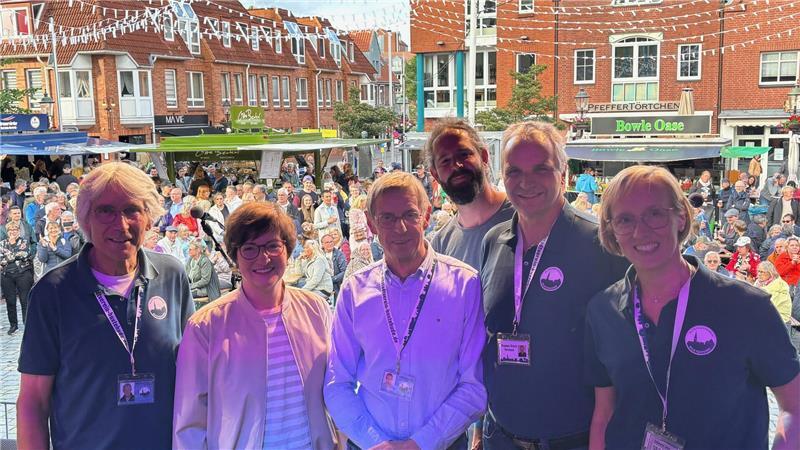 Ehrenamtliche Organisatoren des Altstadtvereins Buxtehude stehen bei der Eröffnung auf dem Petri-Platz zusammen mit der Bürgermeisterin im violetten Licht der Scheinwerfer auf der Bühne: Marktmeister Heinrich Fiege (von links), Bürgermeisterin Katja Oldenburg-Schmidt, 1. Vorsitzender Ulrich Wiegel, Veranstaltungsmanager Nick Reinartz, Koordinator Stephan Schulz und Susanne Tobaben (Büro Altstadtverein).